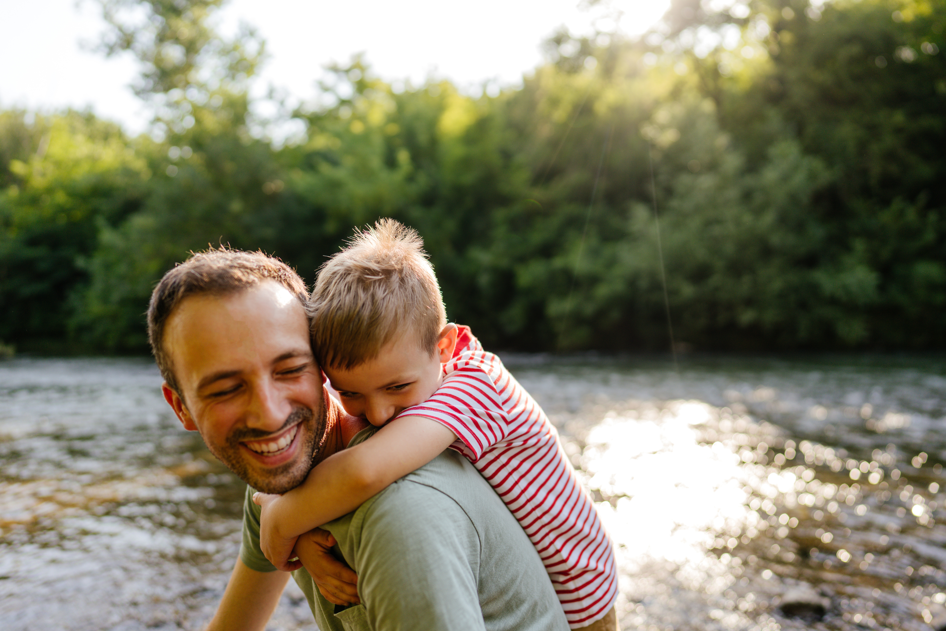 A father and son enjoying a peaceful moment together while wading in a river, surrounded by nature.